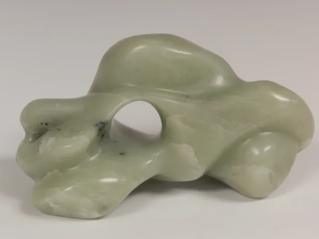 A pale green sculptural form with rounded folds and openings.