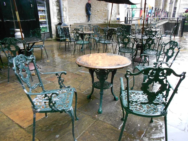 Empty café tables with ornate green chairs on a tiled floor.