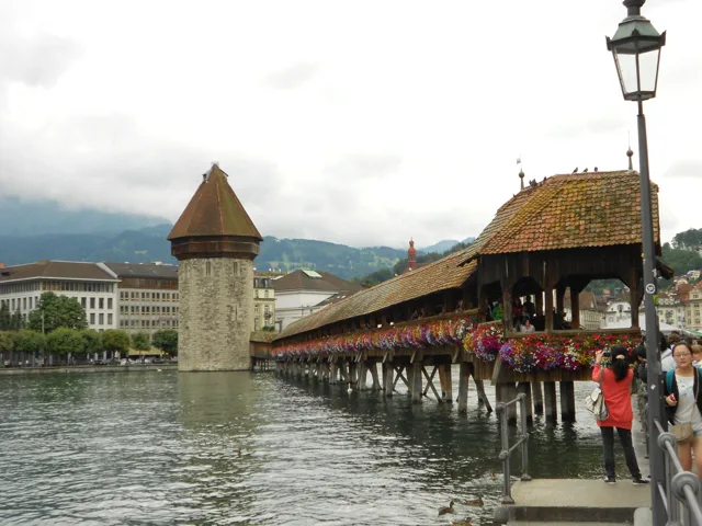 A wooden covered bridge and stone tower spanning a river.