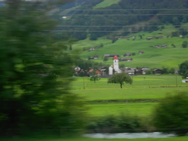 Green fields and hillside houses seen through a moving window.