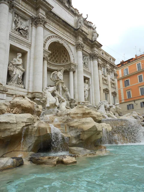 Sculpted figures and rock formations above a turquoise fountain.