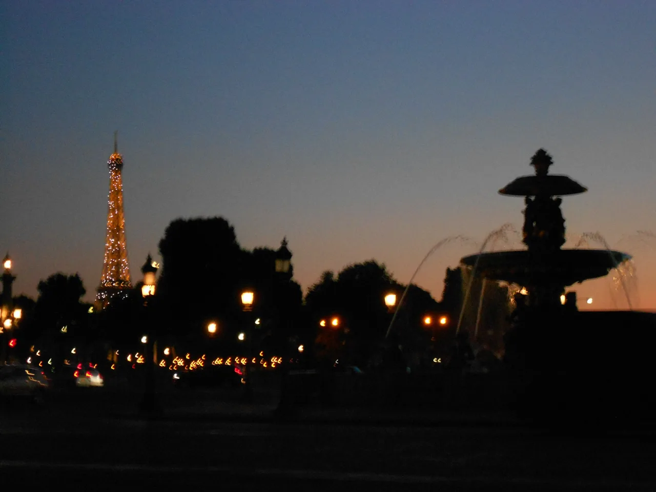 A fountain silhouette and illuminated tower against a twilight sky.