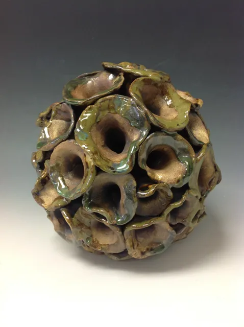 A rounded green and brown sculpture covered in circular openings.