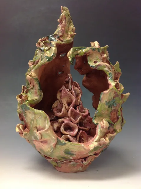 A tall open vessel with textured green edges and curled forms inside.
