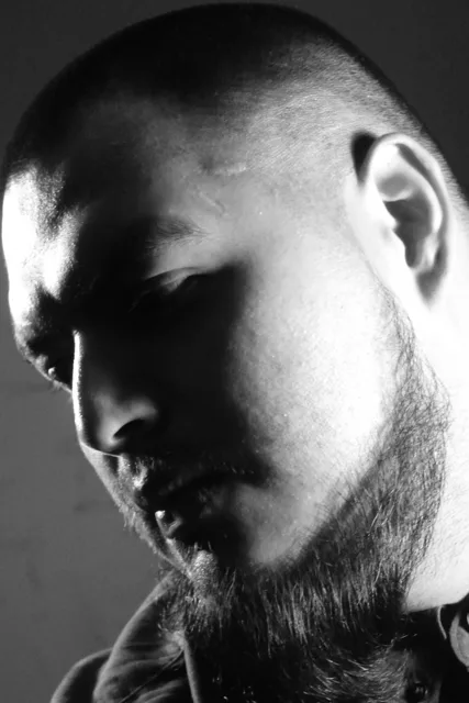 Black-and-white portrait of a bearded face partly in shadow.