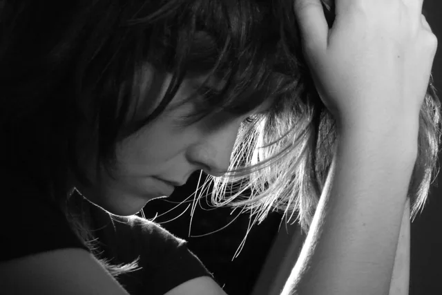 Black-and-white portrait of a person looking down with a hand near their hair.
