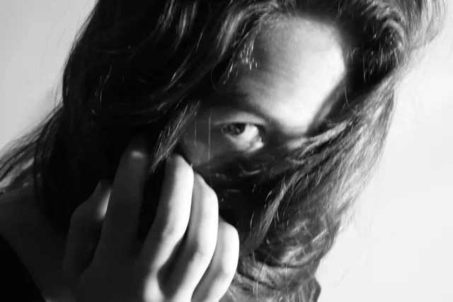 Black-and-white portrait with one eye looking through loose hair.