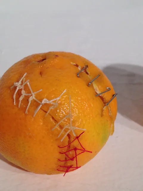 Close-up of an orange peel crossed by colored stitches.