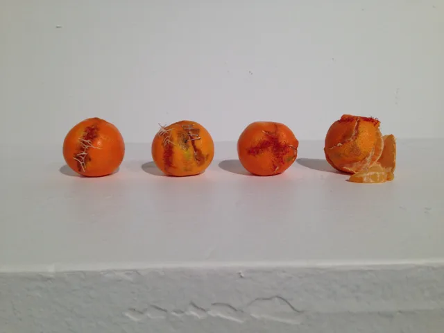 Four altered oranges arranged across a white shelf.