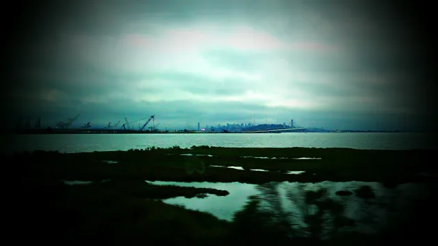 A dark shoreline and bay beneath a band of cloudy sky.