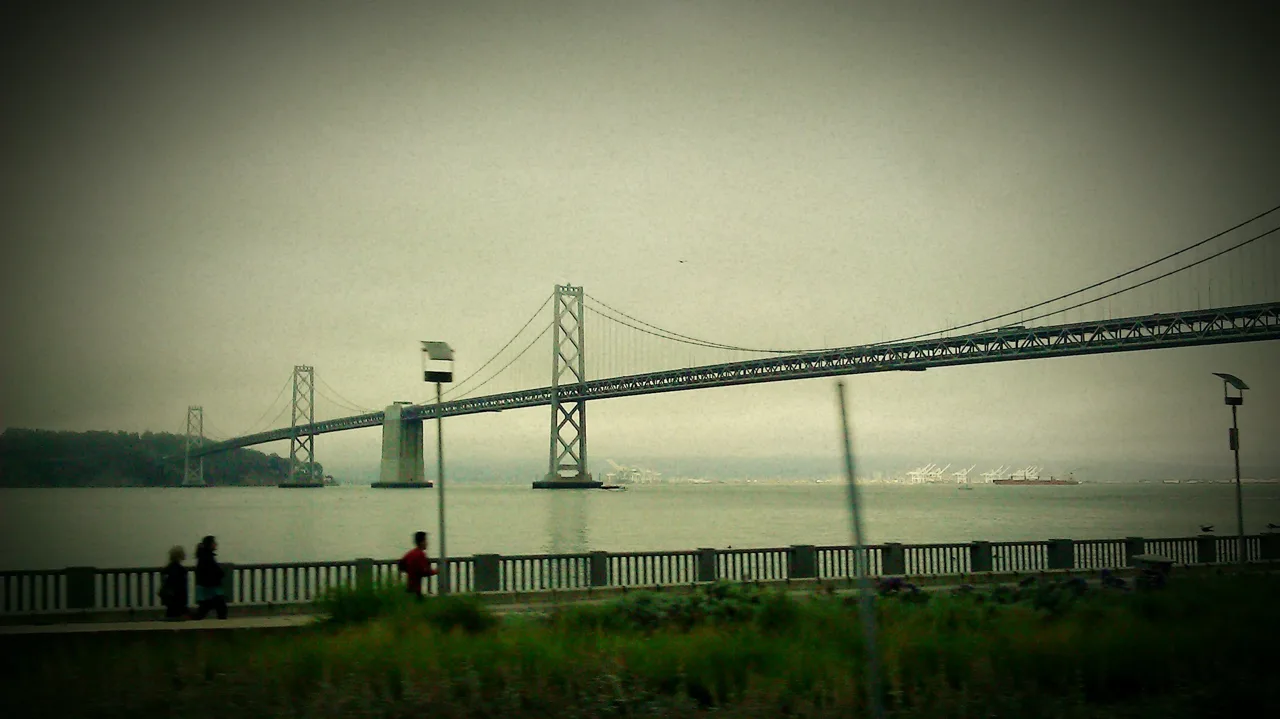 A suspension bridge across the bay, viewed from a waterfront promenade.