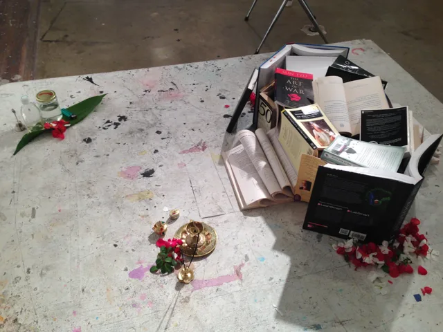 An angled view across a floor installation of books, objects, and petals.